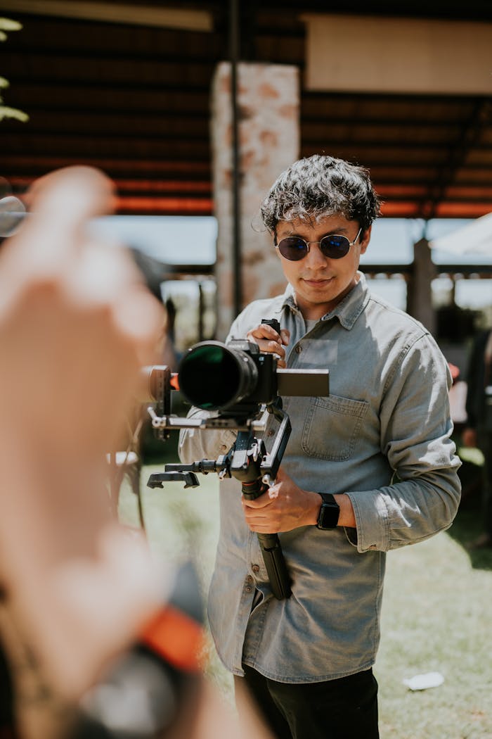 Our Services A male cinematographer using a camera stabilizer outdoors on a sunny day, focused on his subject.